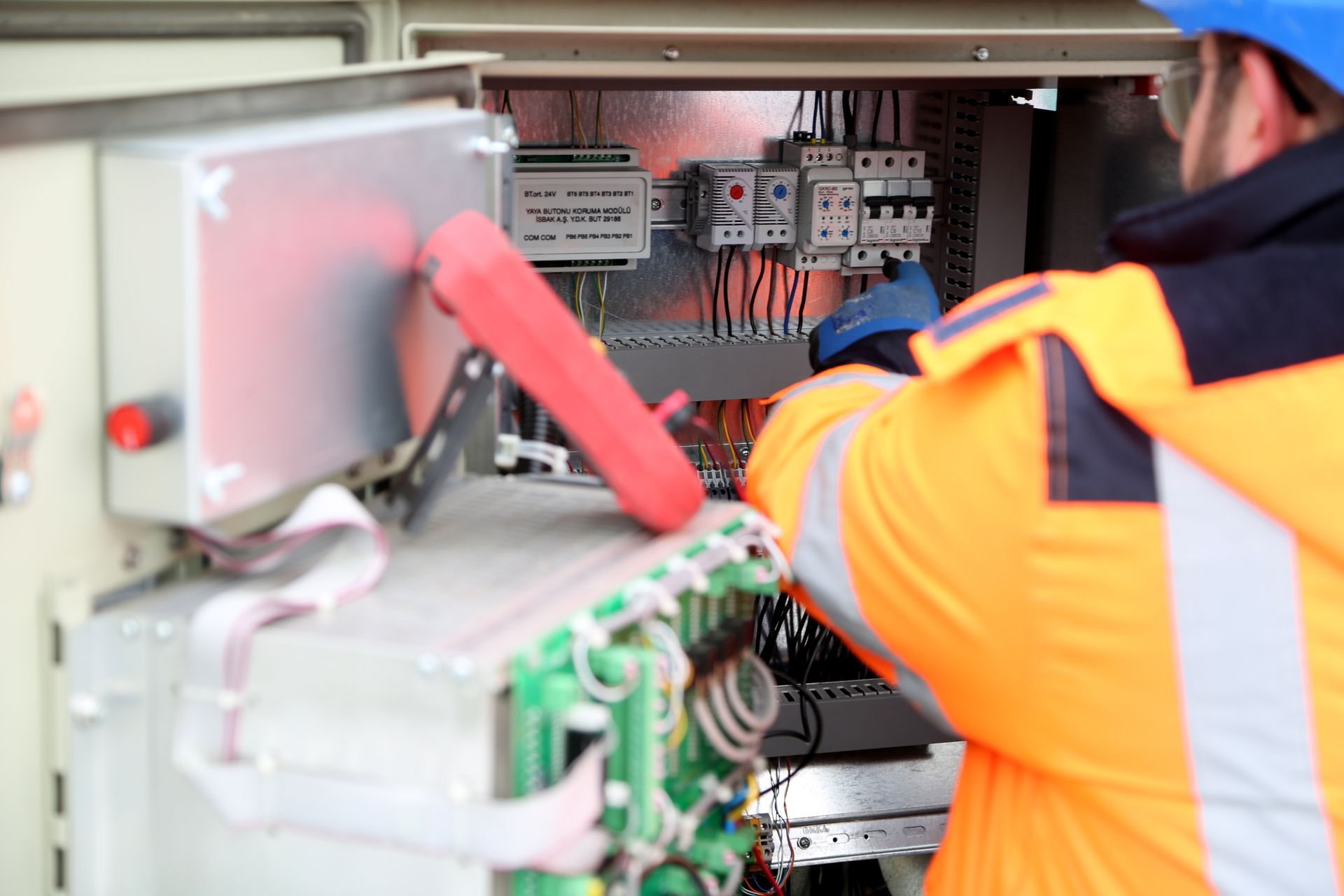 Elektriker i sikkerhedsvest arbejder i et teknikskab med automatsikringer og styringsmoduler